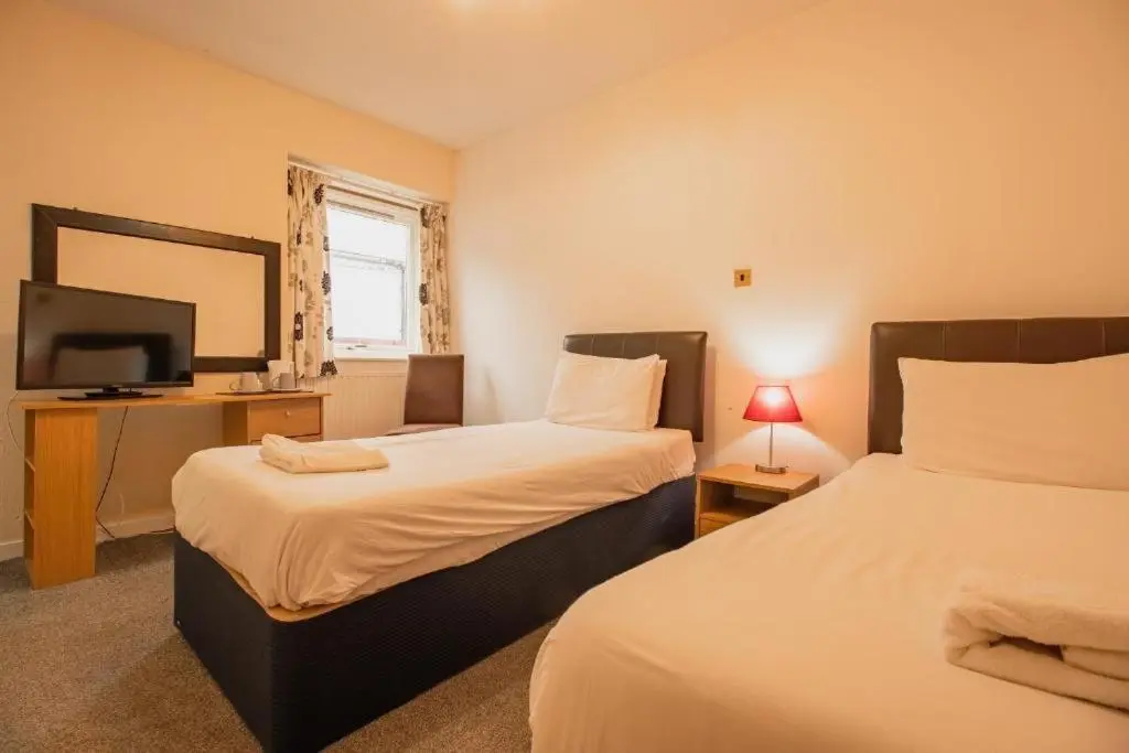 two beds in a room with a tv and a bed sidx sidx sidx at The Ben Mhor Hotel, Bar & Restaurant in Grantown on Spey