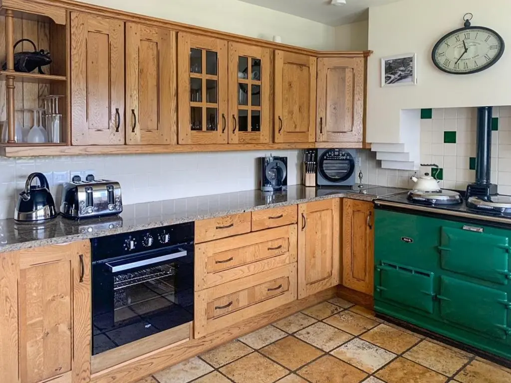 a kitchen with wooden cabinets and a clock on the wall at Sluice Keeper's Cottage in Skelbo