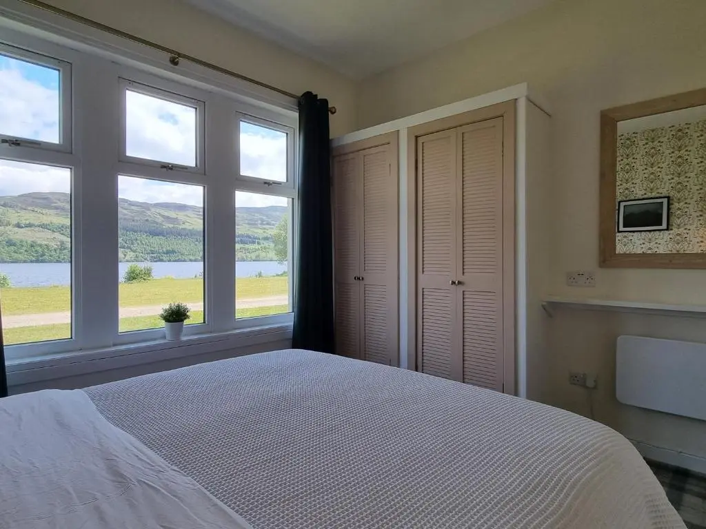 a bedroom with a large bed and two windows at The Apartment at Old Pier House in Fort Augustus