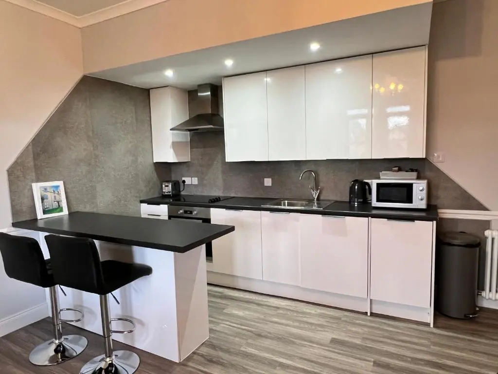 a kitchen with white cabinets and a black counter top at Castle Grant Apartment in Inverness