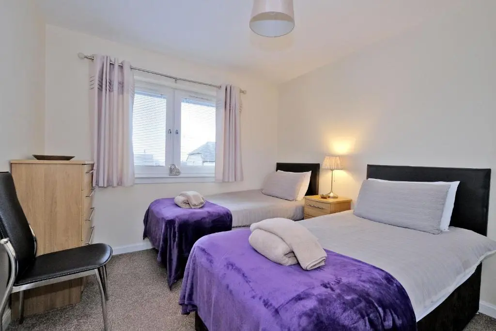 a bedroom with two beds with purple sheets and a window at Caledonia Newhills Apartment in Aberdeen