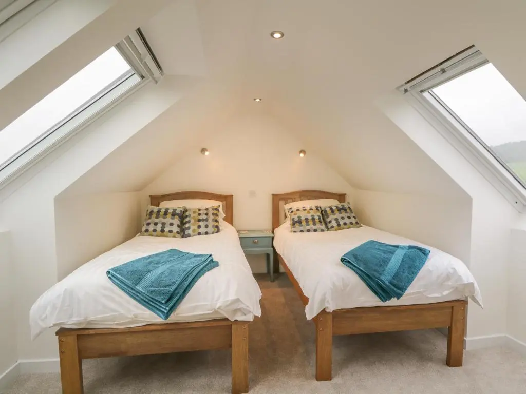 two beds in a attic bedroom with two windows at Enzie Station Cottage in Buckie