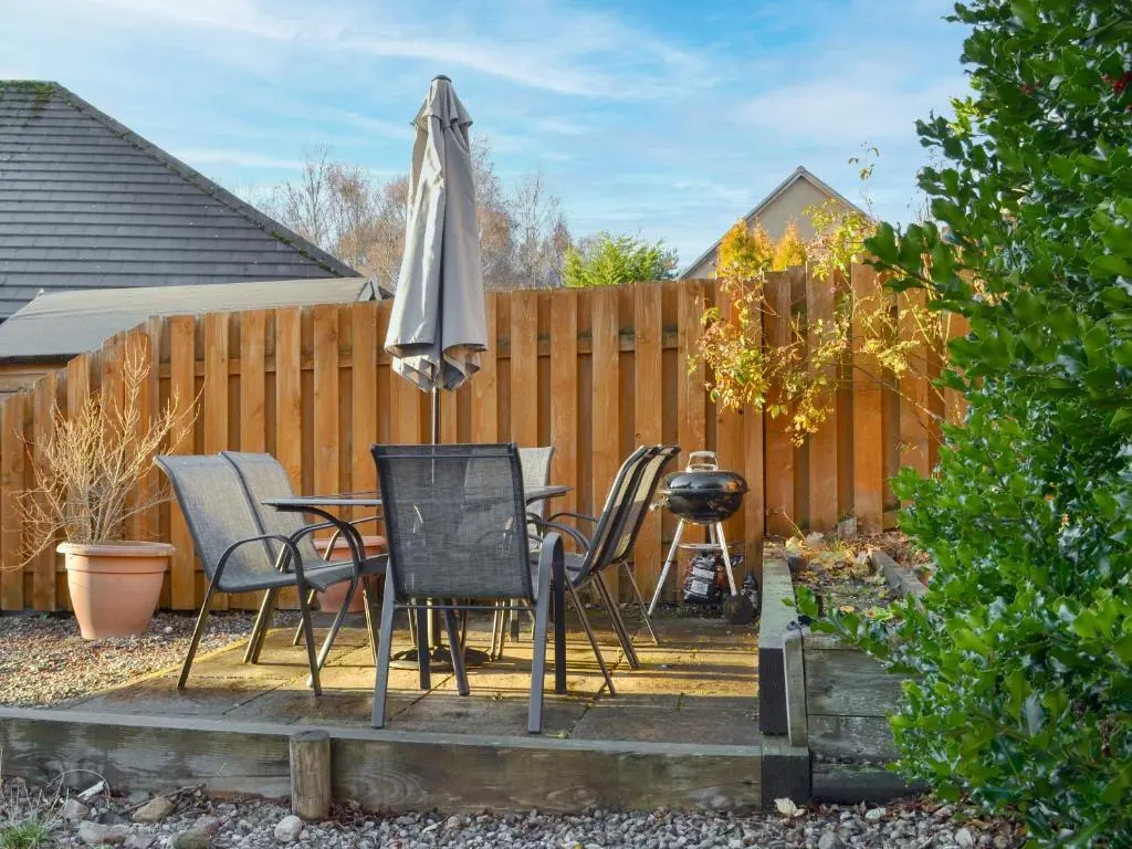 a patio with a table and an umbrella and chairs at Uaine Cottage in Aviemore