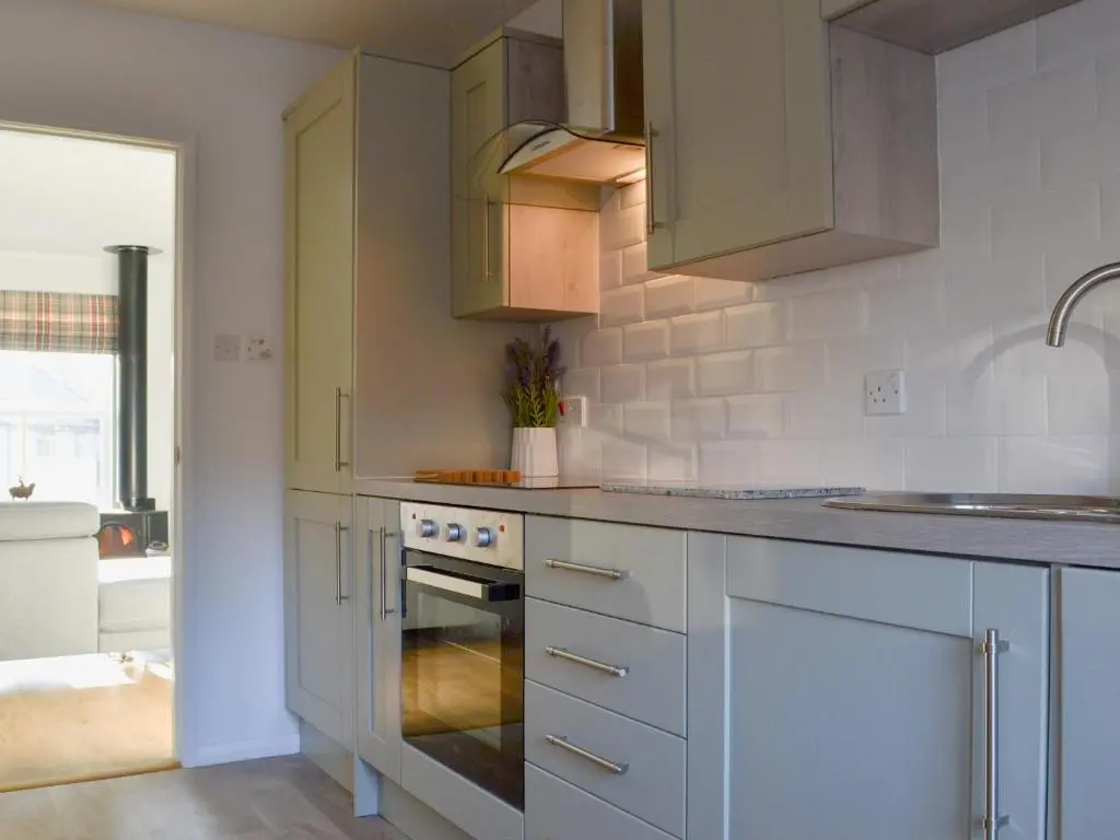 a kitchen with white cabinets and a stove top oven at Uaine Cottage in Aviemore
