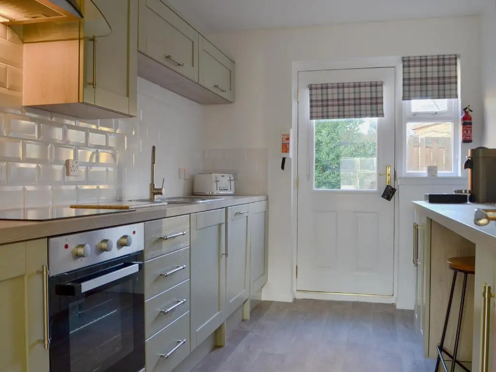 a kitchen with white cabinets and a white door at Uaine Cottage in Aviemore