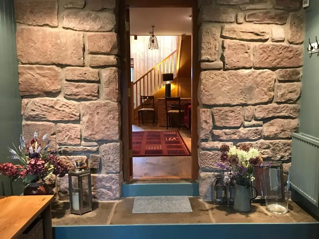 a stone wall with a door into a room with flowers at Highfield House in Dornoch