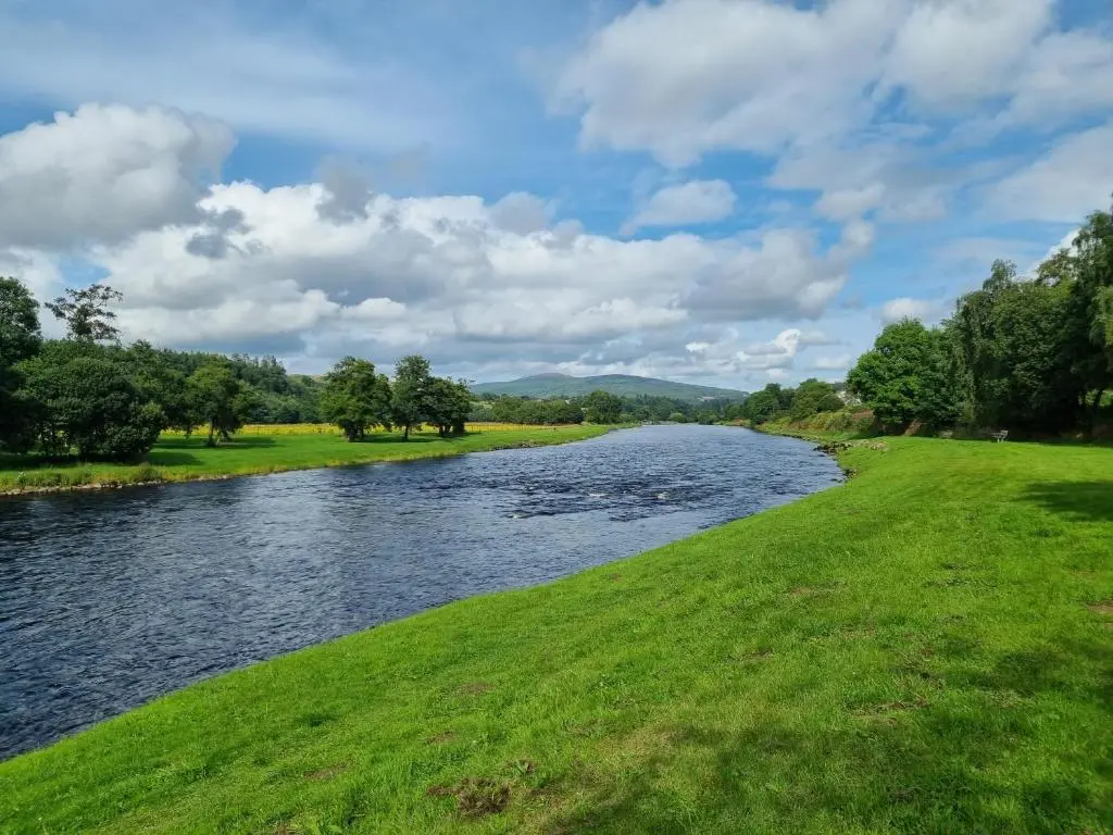 a river with a grassy field next to it at The Coal Office Aberlour in Aberlour