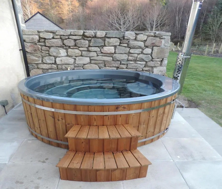 a hot tub in a yard with a stone wall at Rowan House in Inveran