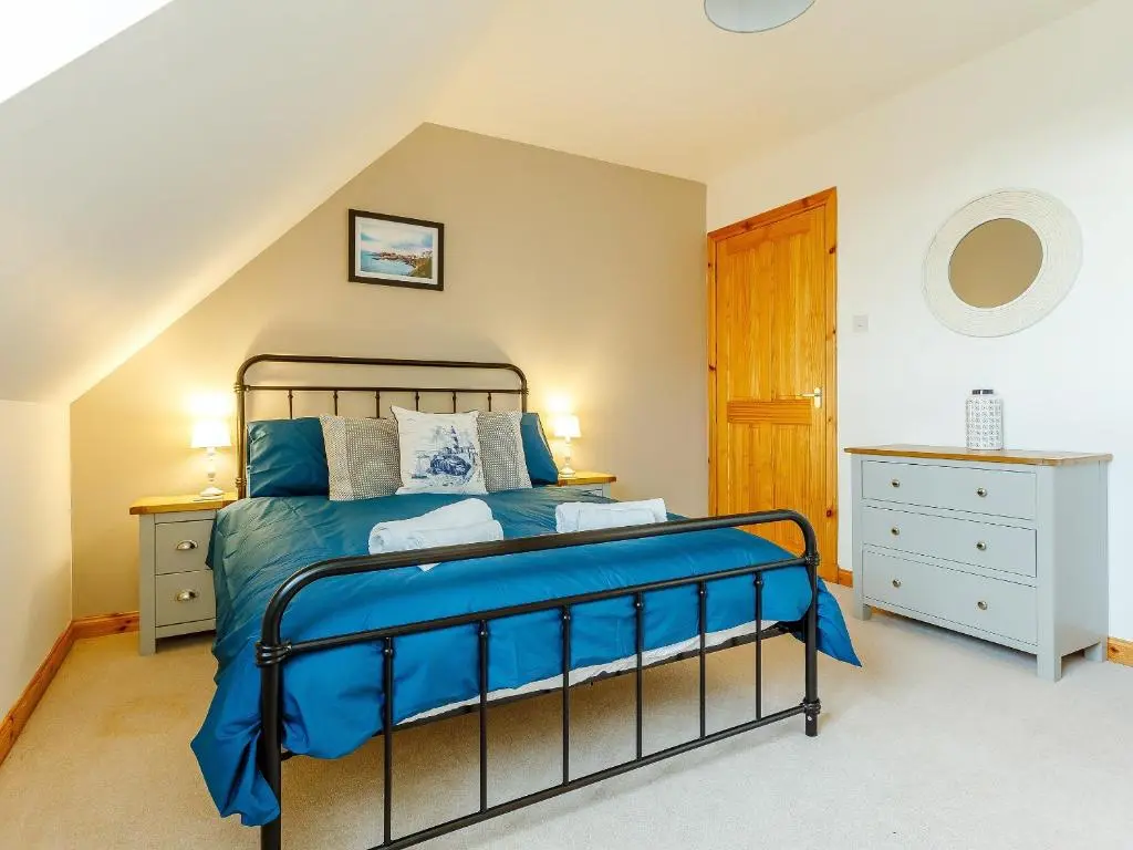 a bedroom with a bed with blue sheets and a wooden door at The Big Hoose in Achnahanat