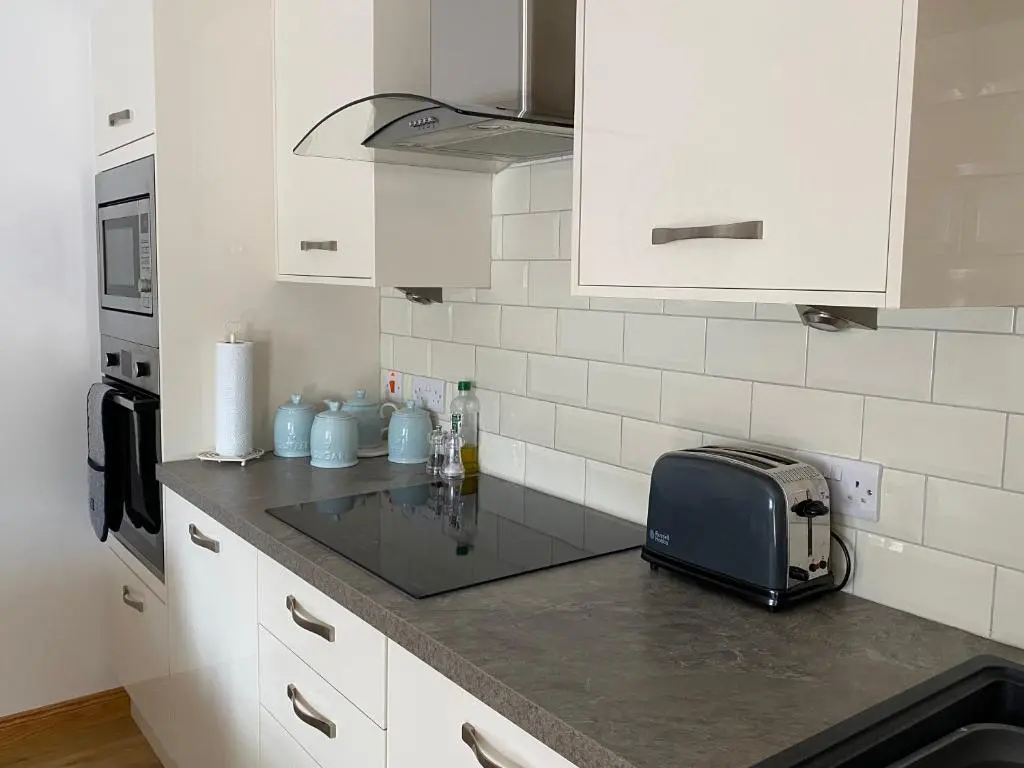 a kitchen with white cabinets and a toaster on a counter at The Den in Stuartfield