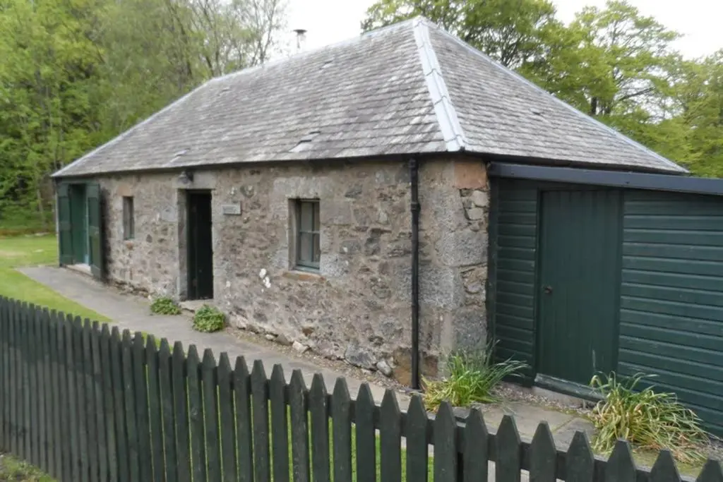 an old stone building with a green garage at Blairbeg Cottage in Blairgowrie