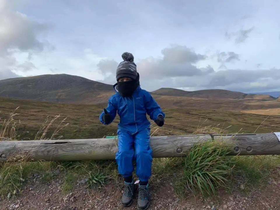 a child is sitting on a log in a field at The One - Chalet in the Cairngorms in Boat of Garten
