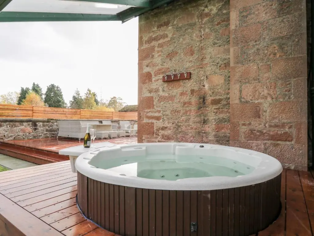 a hot tub on a deck with a brick wall at Orrinside in Muir of Ord