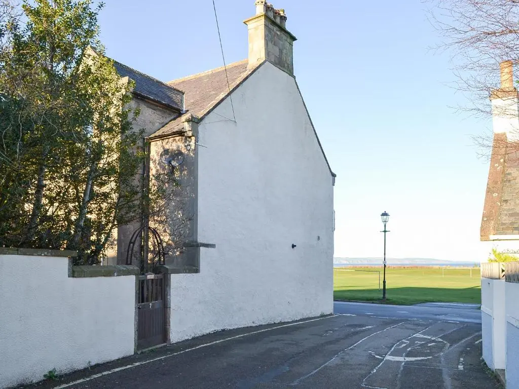 an old white building with a tower on a street at Brighton House in Nairn