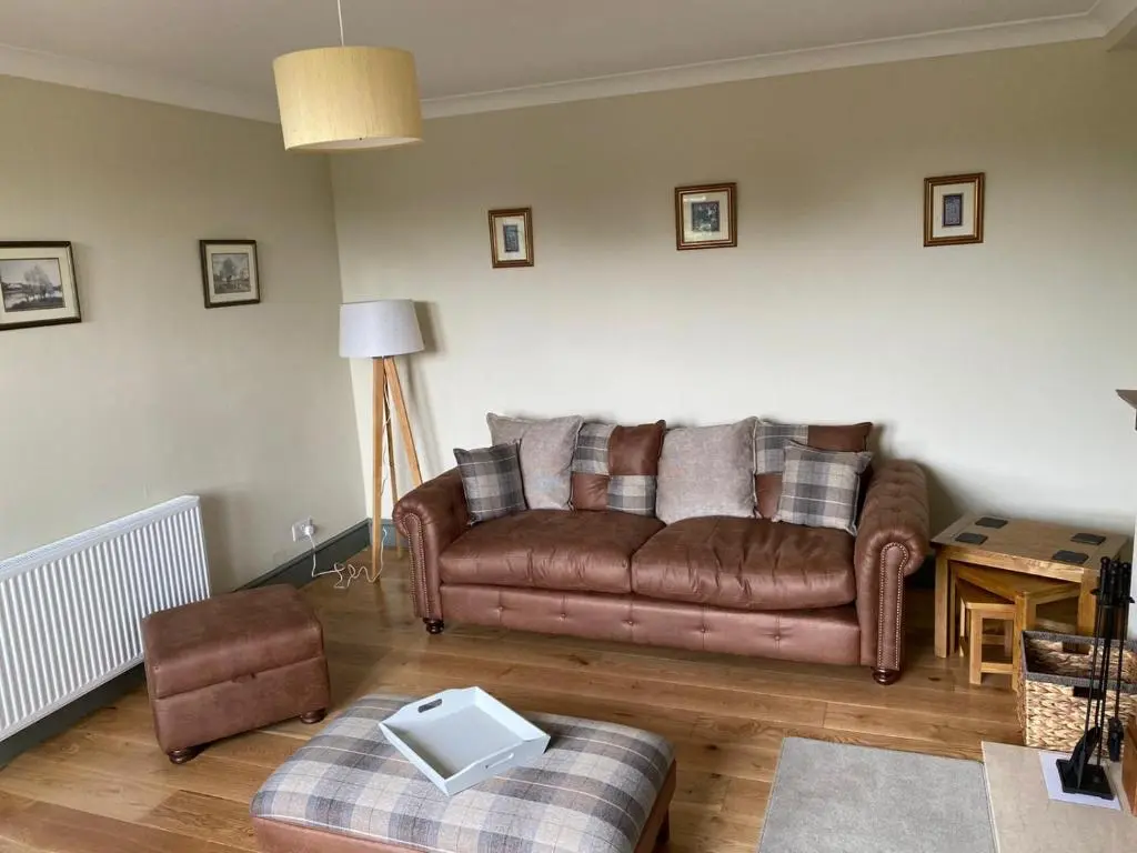 a living room with a brown couch and a chair at Granite Cottage in Nethy Bridge