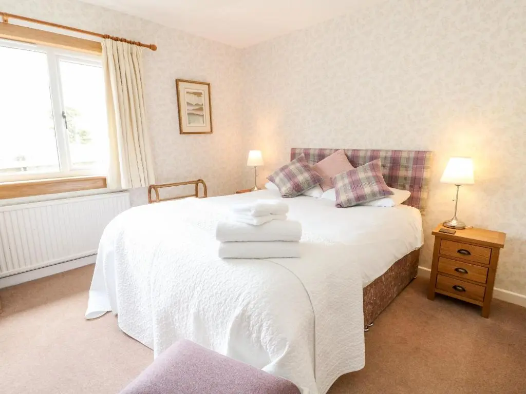 a bedroom with a white bed with towels on it at Beechwood Cottage in Pitlochry