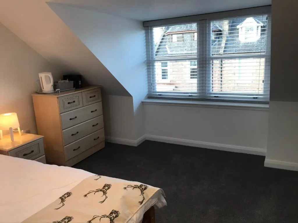 a bedroom with a bed and a dresser and a window at Thistle House in Inverness