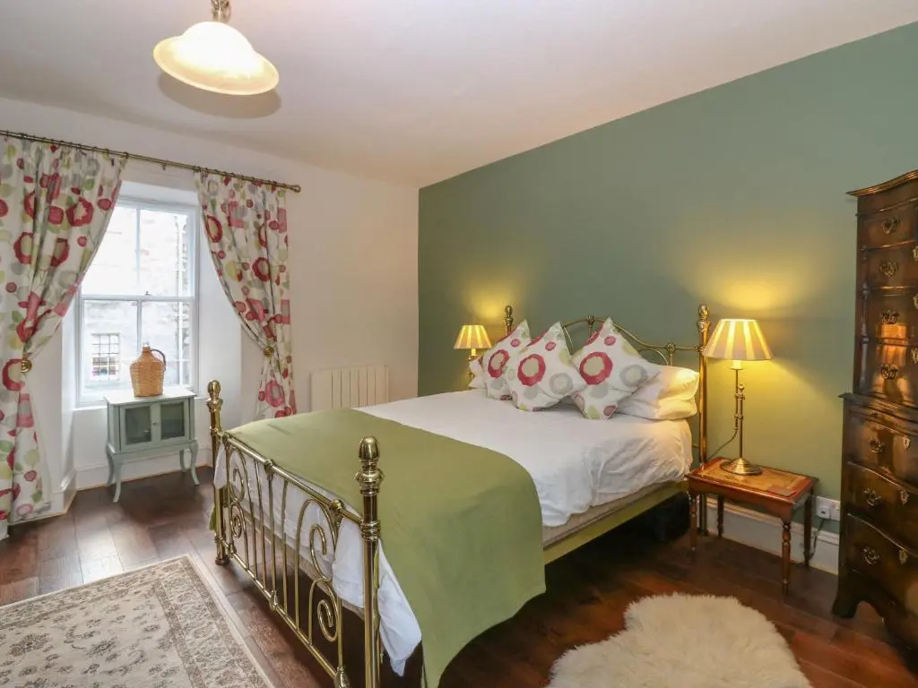 a bedroom with a bed with a green blanket and pillows at Courtyard Cottage - Drum Castle in Banchory
