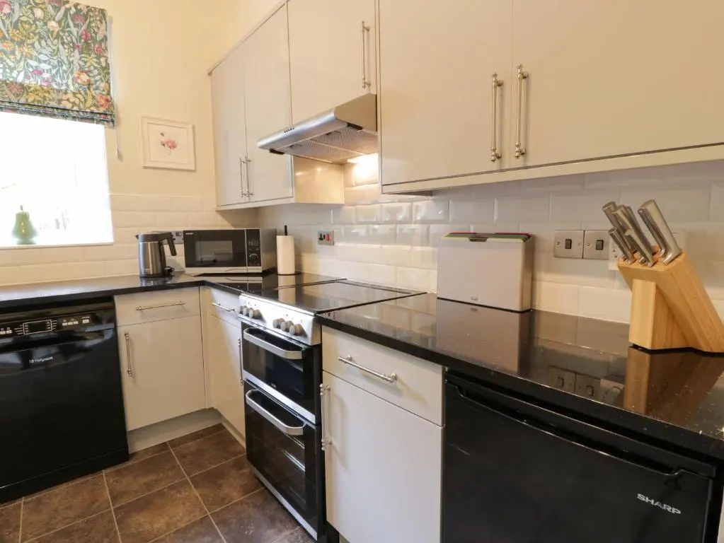 a kitchen with white cabinets and black appliances at East Lodge - Crathes Castle in Banchory