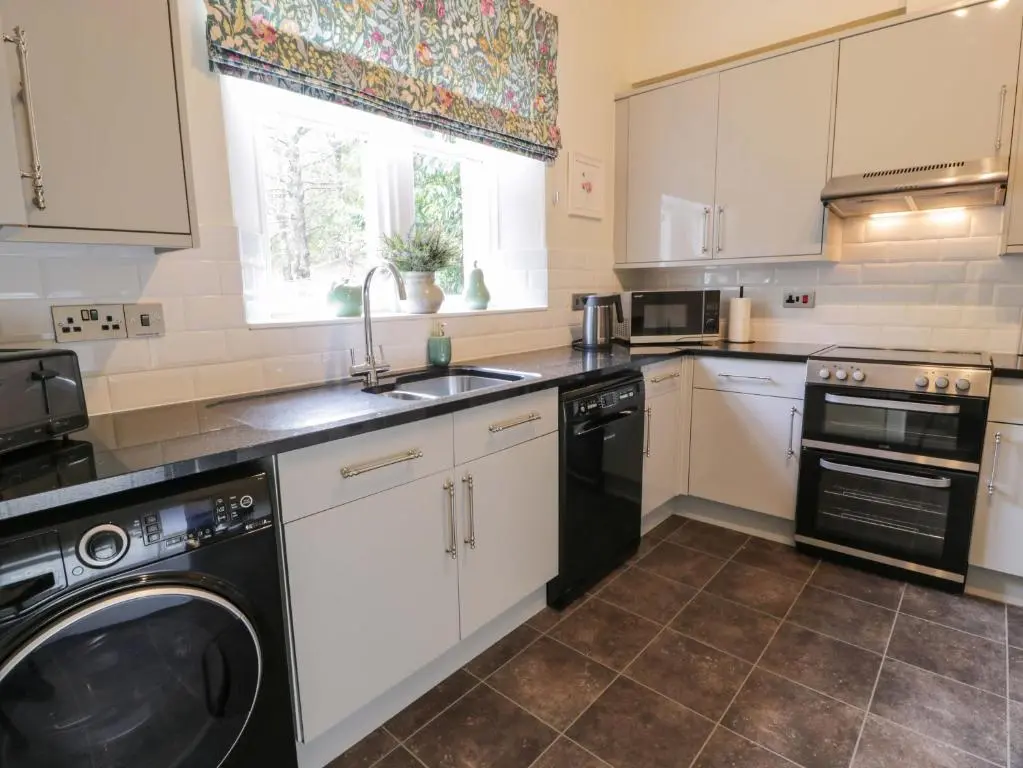 a kitchen with white cabinets and a black dishwasher at East Lodge - Crathes Castle in Banchory