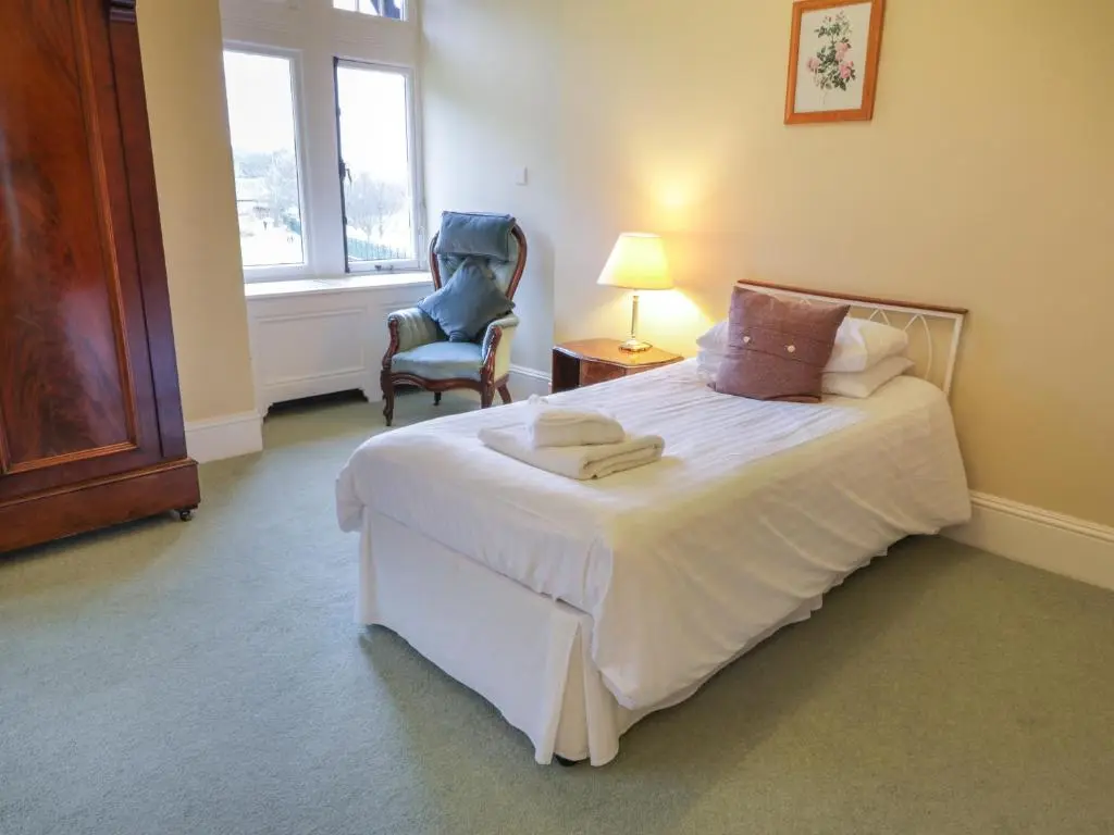 a bedroom with a large white bed and a chair at Bynack - Mar Lodge Estate in Ballater
