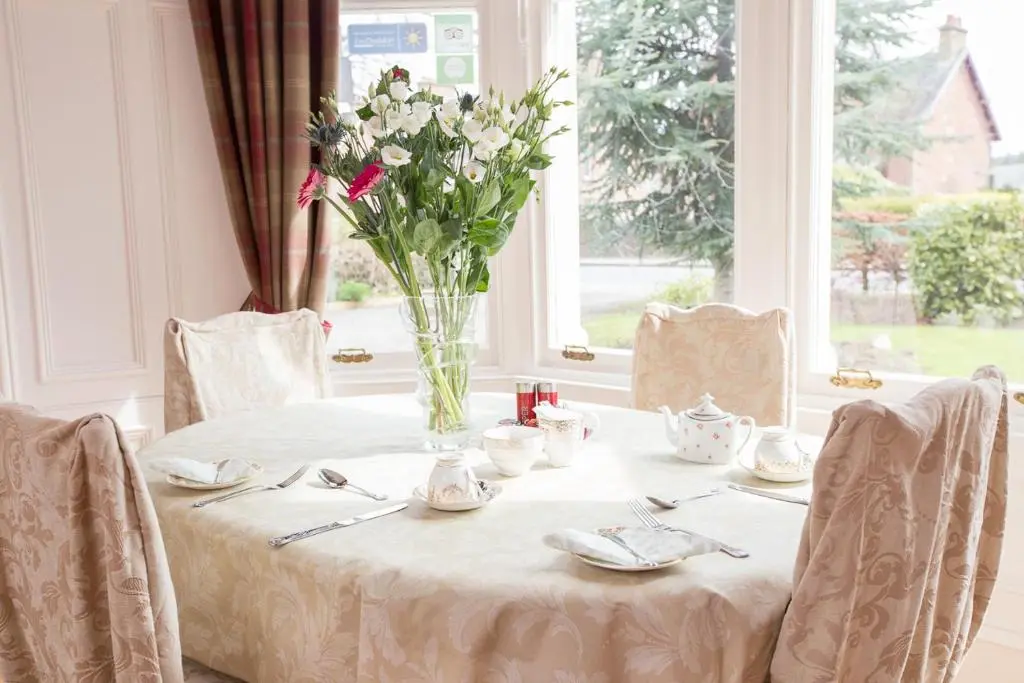 a white table with a vase of flowers on it at Chrialdon House in Beauly