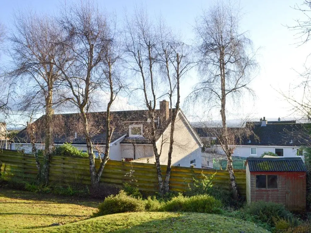 a fence in a yard with trees and houses at Wester Links in Fortrose