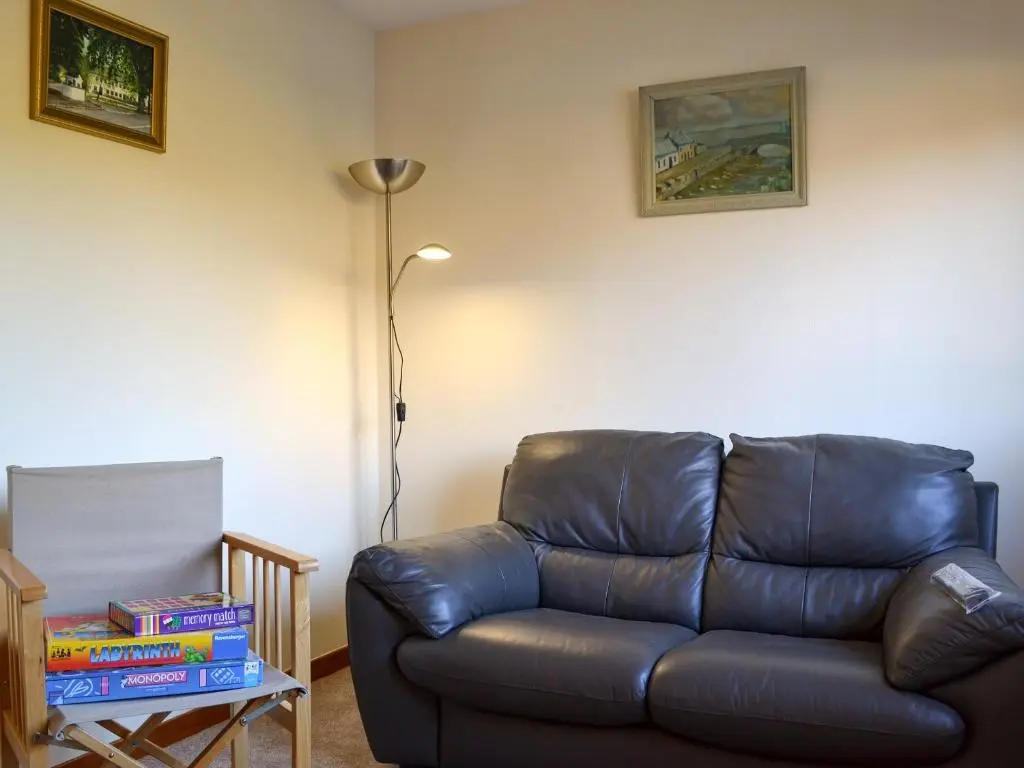 a living room with a leather couch and a lamp at Wester Links in Fortrose