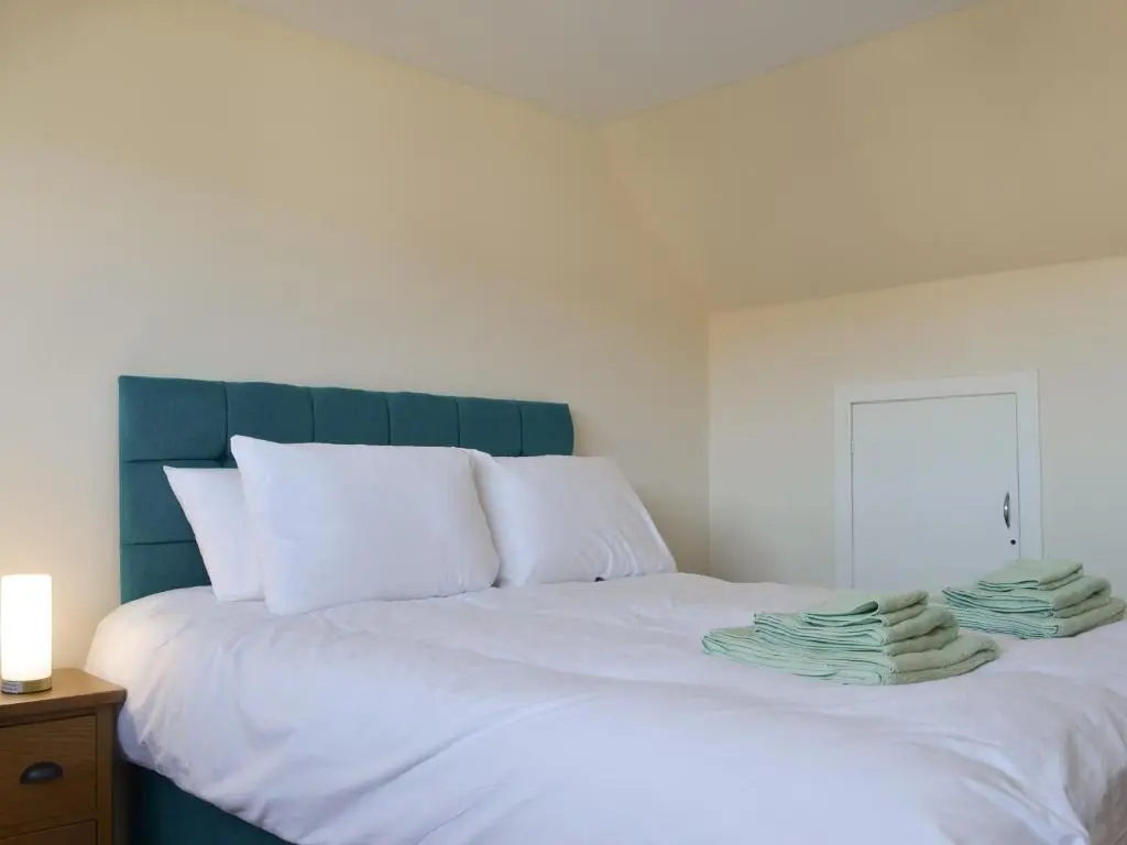 a white bed with white pillows and a blue headboard at Wester Links in Fortrose