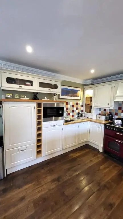 a large kitchen with white cabinets and wooden floors at Red Squirrel Lodge in Boat of Garten