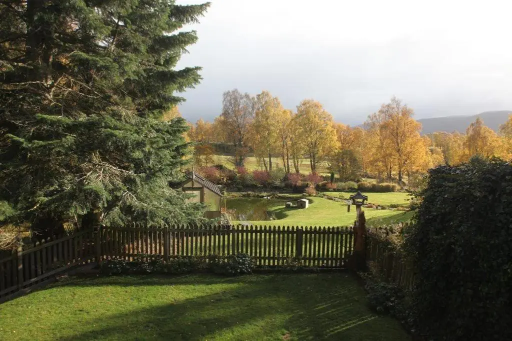 a fence in front of a yard with a golf course at Red Squirrel Lodge in Boat of Garten