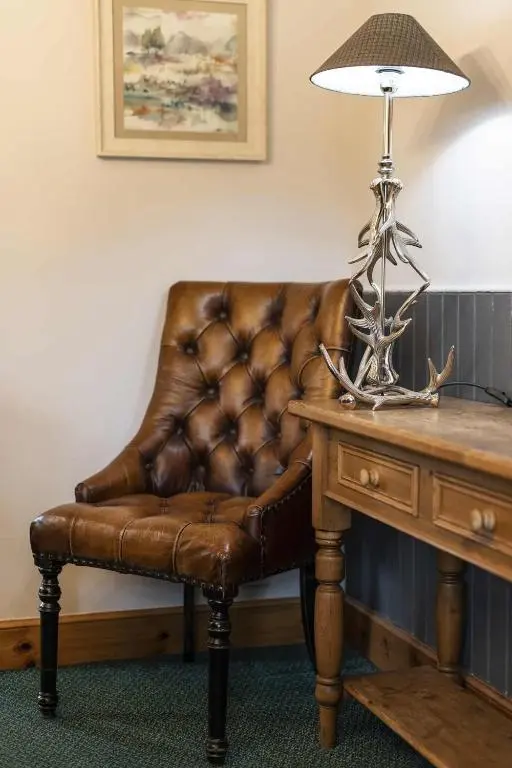 a brown leather chair sitting next to a table with a lamp at Rowan Cottage in Aviemore