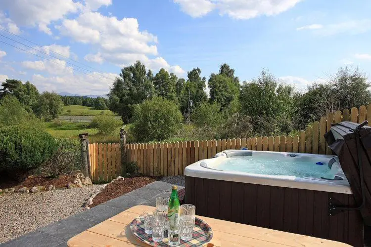 a hot tub in a backyard with a wooden fence at Rowan Cottage in Aviemore