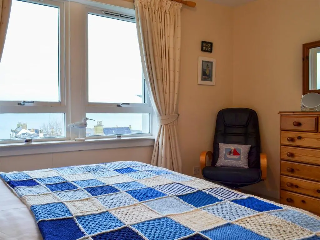 a bedroom with a bed and a chair and windows at Brae Lodge in Cullen