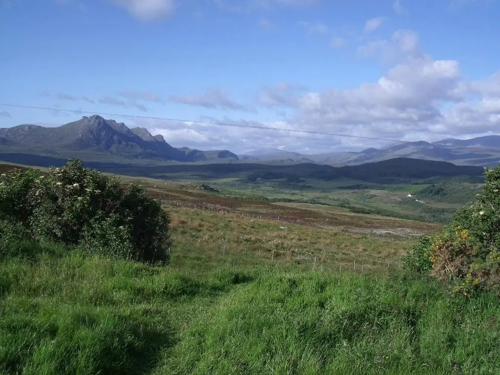 a field of grass with mountains in the background at The Barn in Lairg