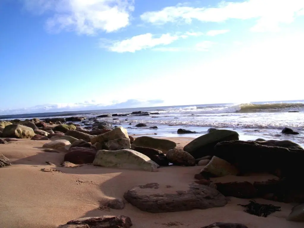 a beach with rocks on the sand and the water at The Barn in Lairg