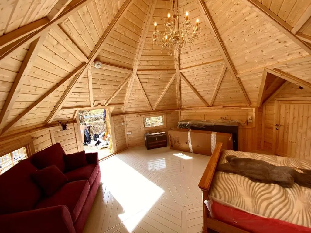 an attic room with a couch and a chandelier at Woodland Lodge Mither Tap in Kintore