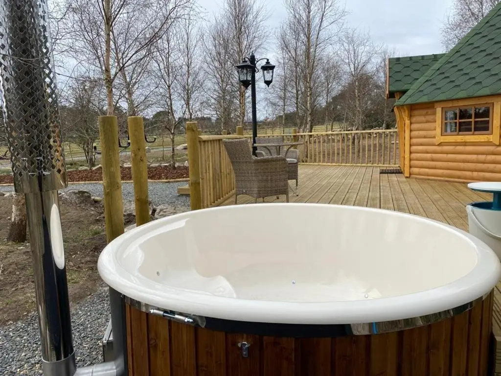 a large bath tub sitting on a deck next to a cabin at Woodland Lodge Oxen Craig in Kintore