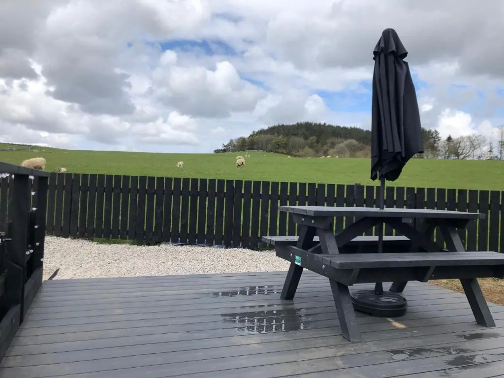 a picnic table with an umbrella next to a fence at Bruxie Holiday Cottages - Honeysuckle Cottage in Maud