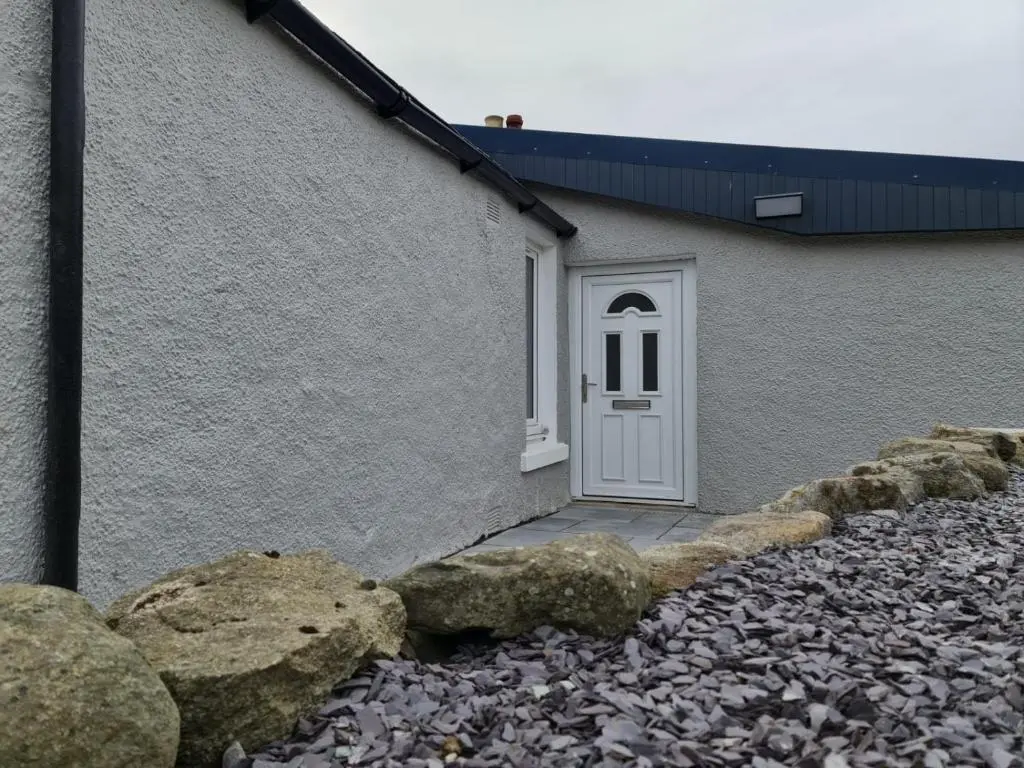a building with a white door and some rocks at Bruxie Holiday Cottages - Honeysuckle Cottage in Maud