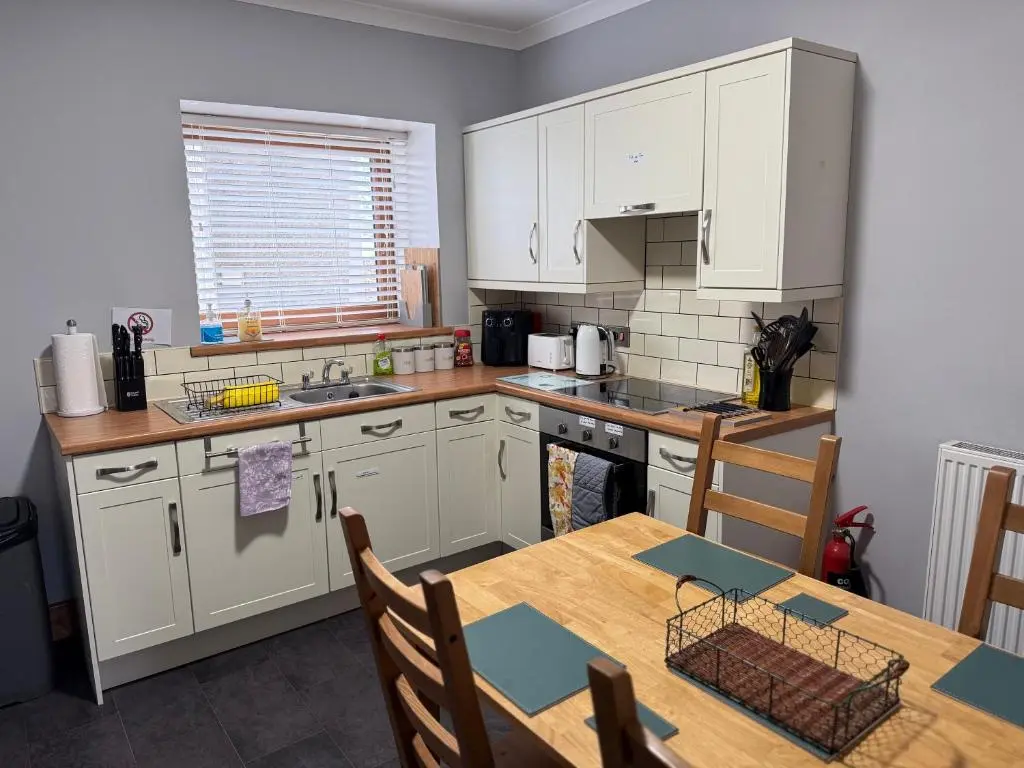 a kitchen with white cabinets and a wooden table at Newly Refurbished 2 Bedroom flat on NC500 route in Wick