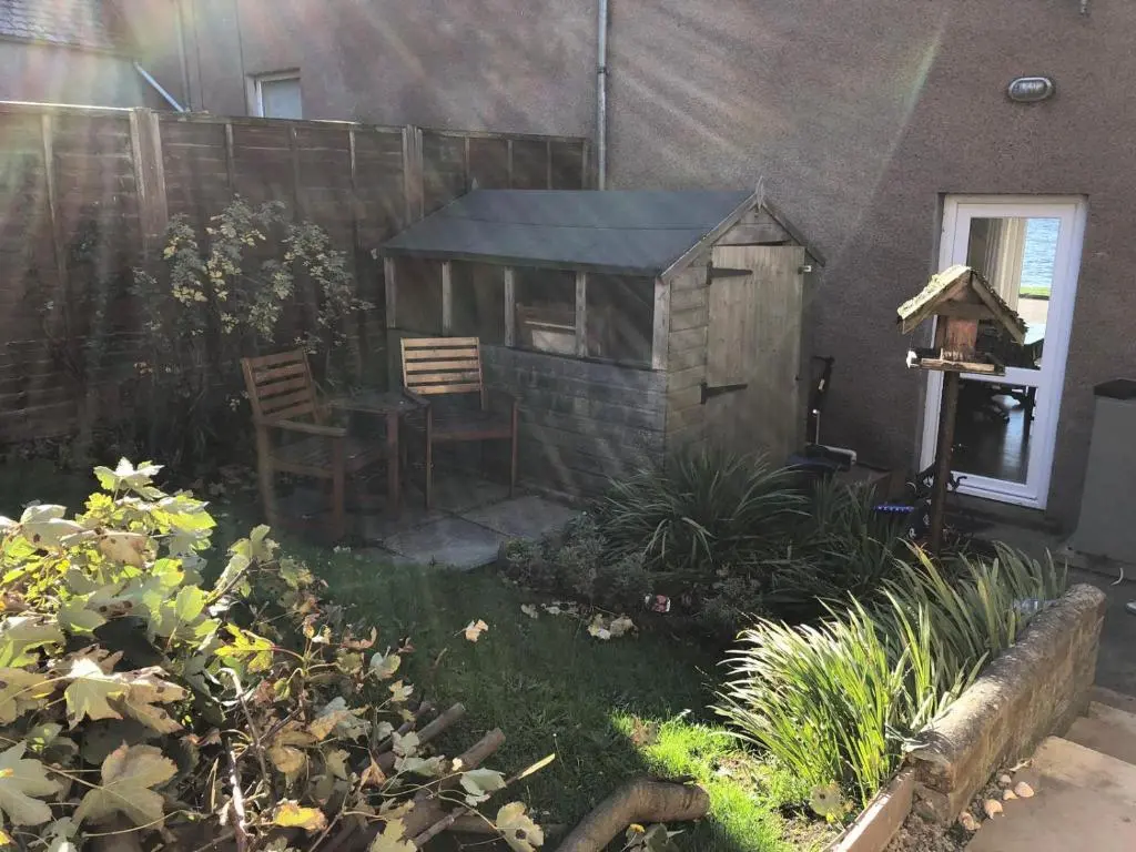 a garden with a wooden shed and a table and chairs at PetFriendly-Beachfront-SunsetFacingSunPorch-Garden in Portmahomack