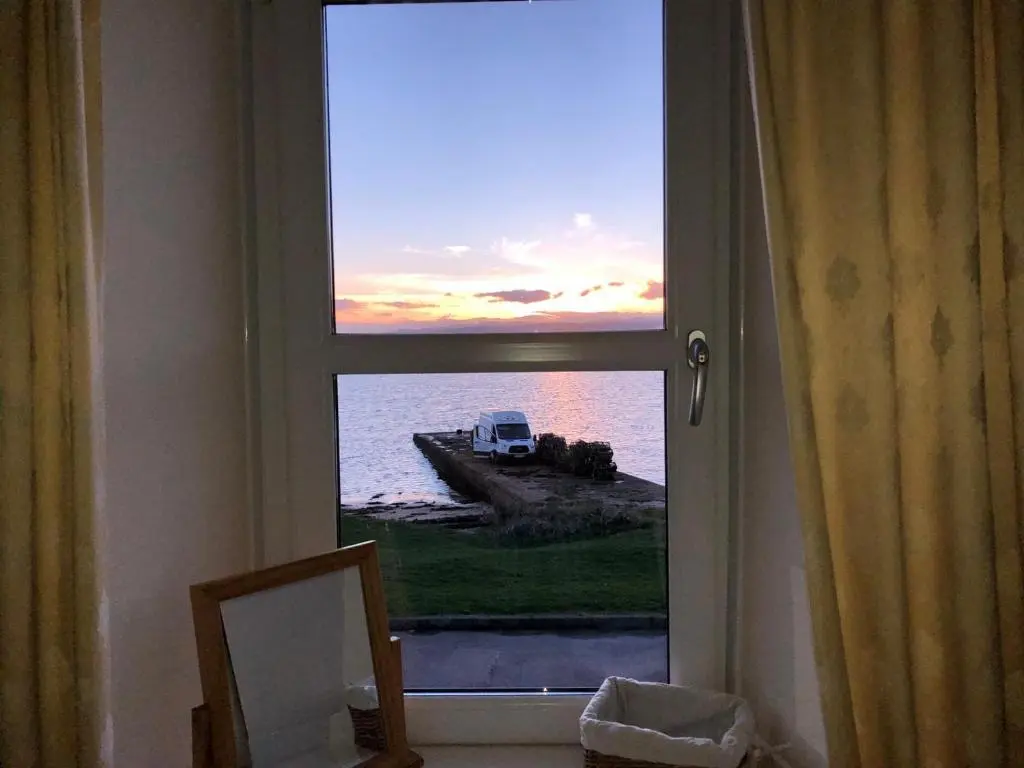 a window with a view of the ocean and a truck at PetFriendly-Beachfront-SunsetFacingSunPorch-Garden in Portmahomack