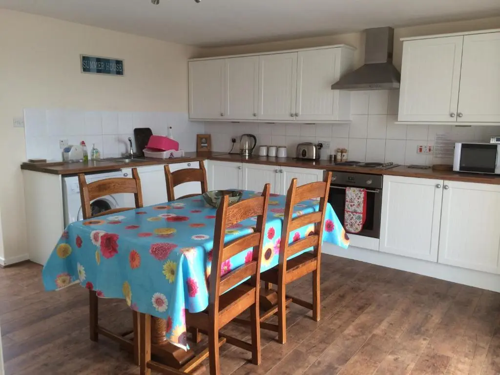 a kitchen with a table and chairs and a kitchen with white cabinets at PetFriendly-Beachfront-SunsetFacingSunPorch-Garden in Portmahomack