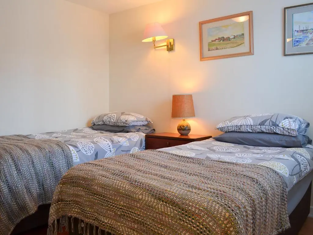 a bedroom with two beds and a lamp on a table at Bruich Cottage in Newtonmore