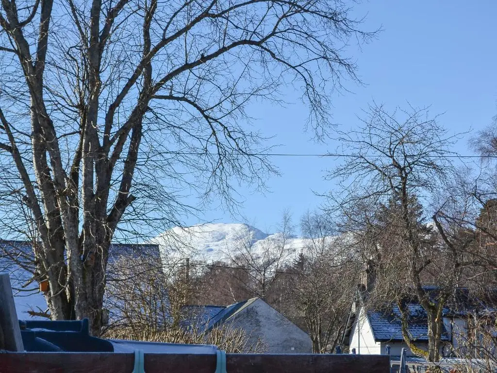 a snow covered mountain in the distance with houses and trees at Bruich Cottage in Newtonmore