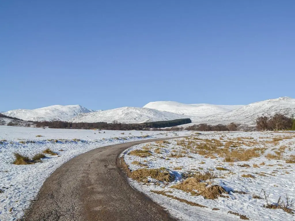 a dirt road in a snowy field with snow covered mountains at Bruich Cottage in Newtonmore