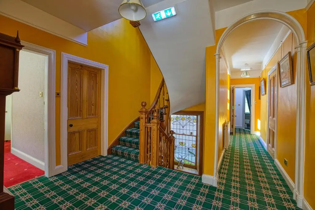 a hallway with yellow walls and a staircase with green tiles at Woodlands Bed and Breakfast in Dornoch