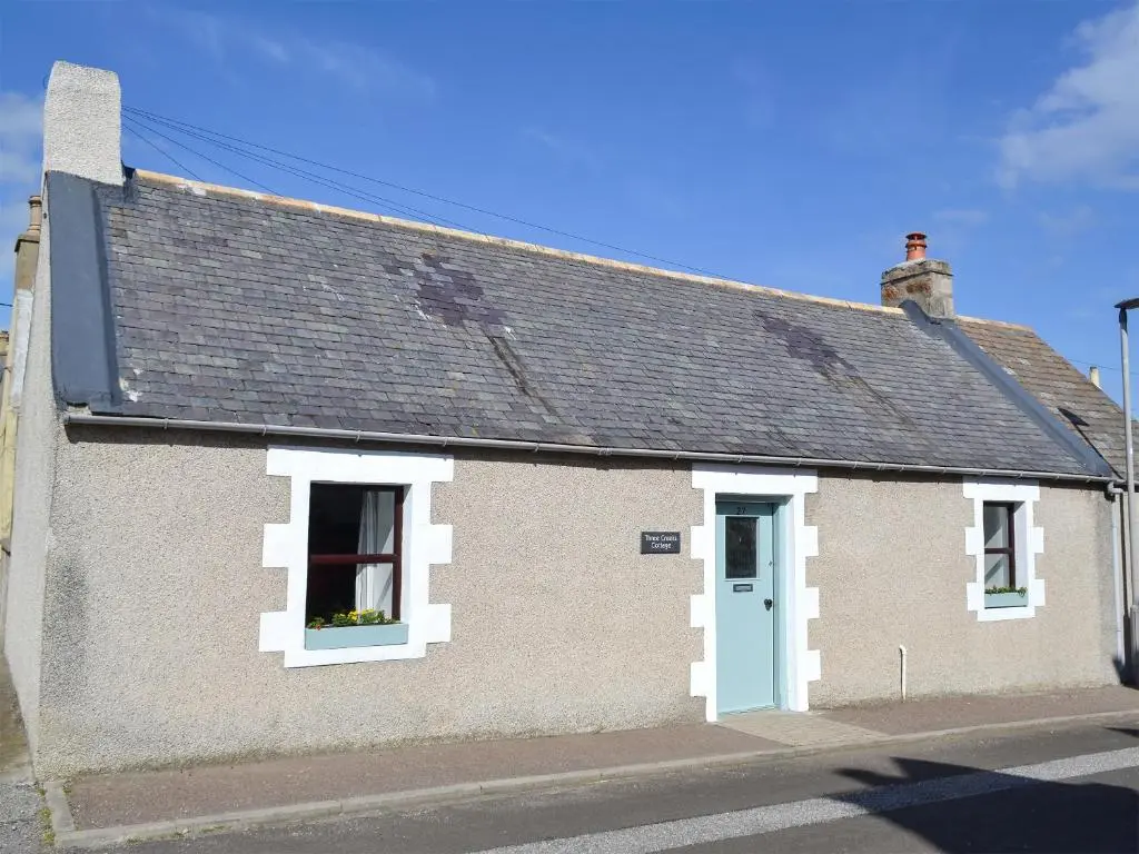 a house with a blue door and a window at Three Creeks Cottage in Portknockie