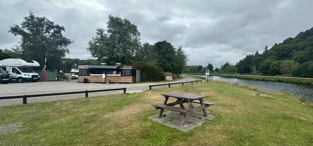 a picnic table sitting in the grass next to a river at Self-Catering Lodge with Hot Tub in Inverness